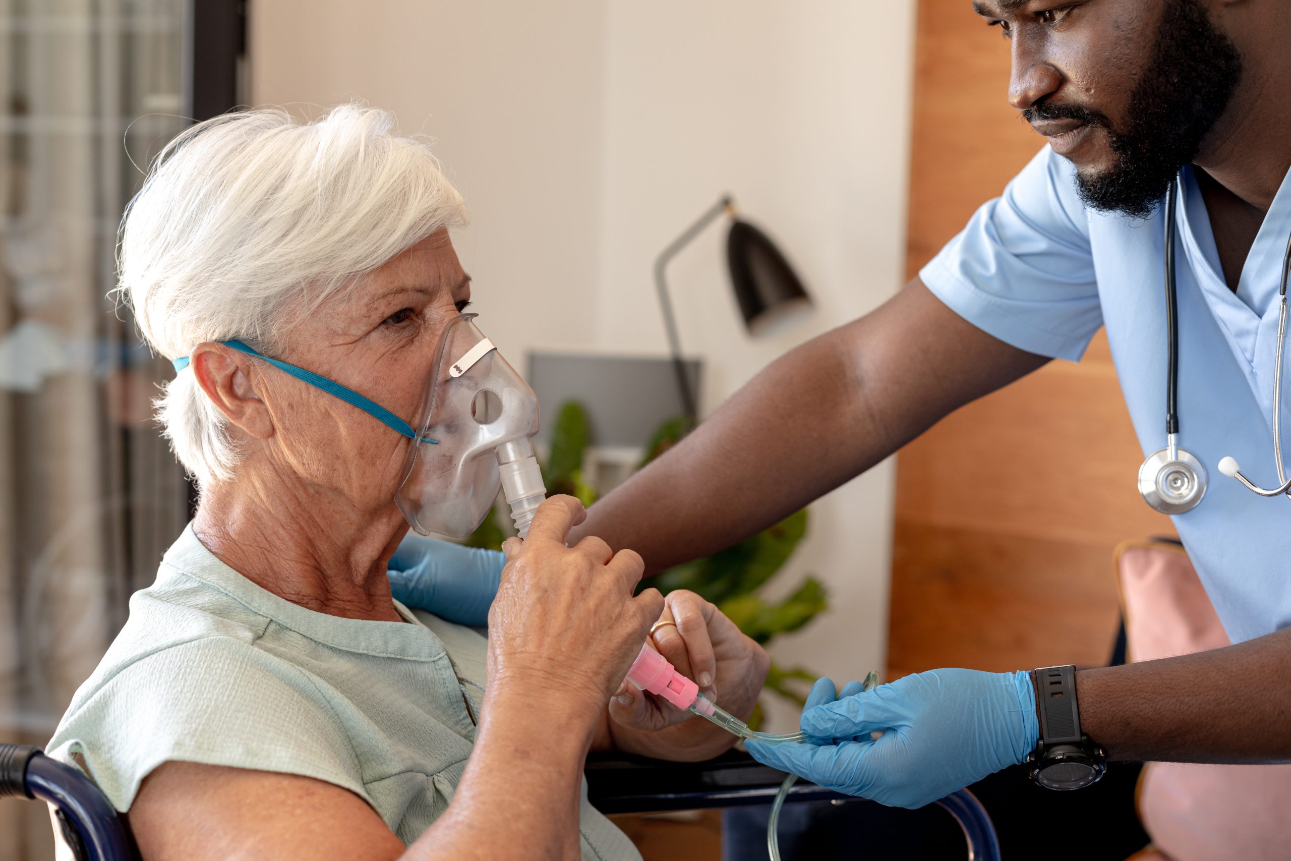 African american male health worker helping caucasian senior woman to use oxygen mask. Medical care and retirement senior lifestyle concept