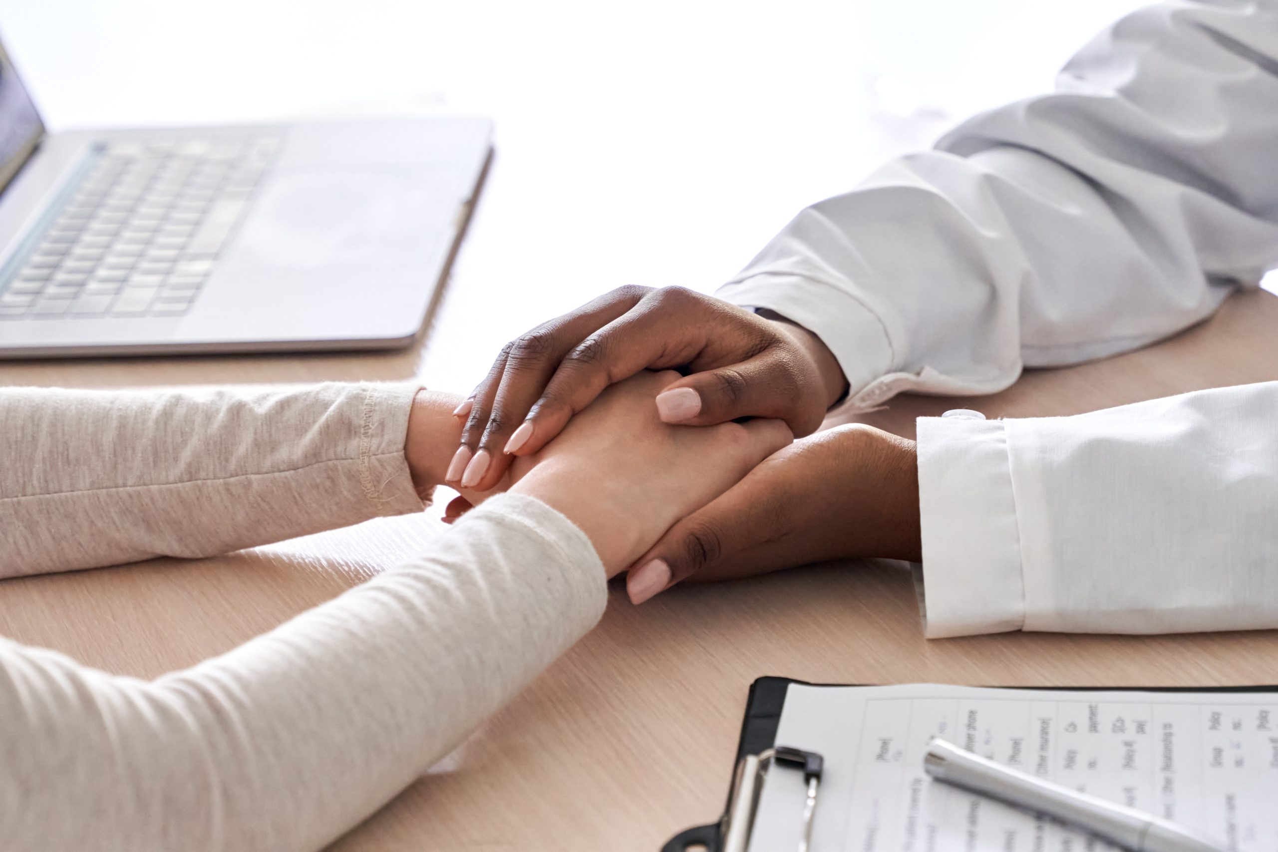 African female doctor holding hand supporting caucasian patient, close up view.