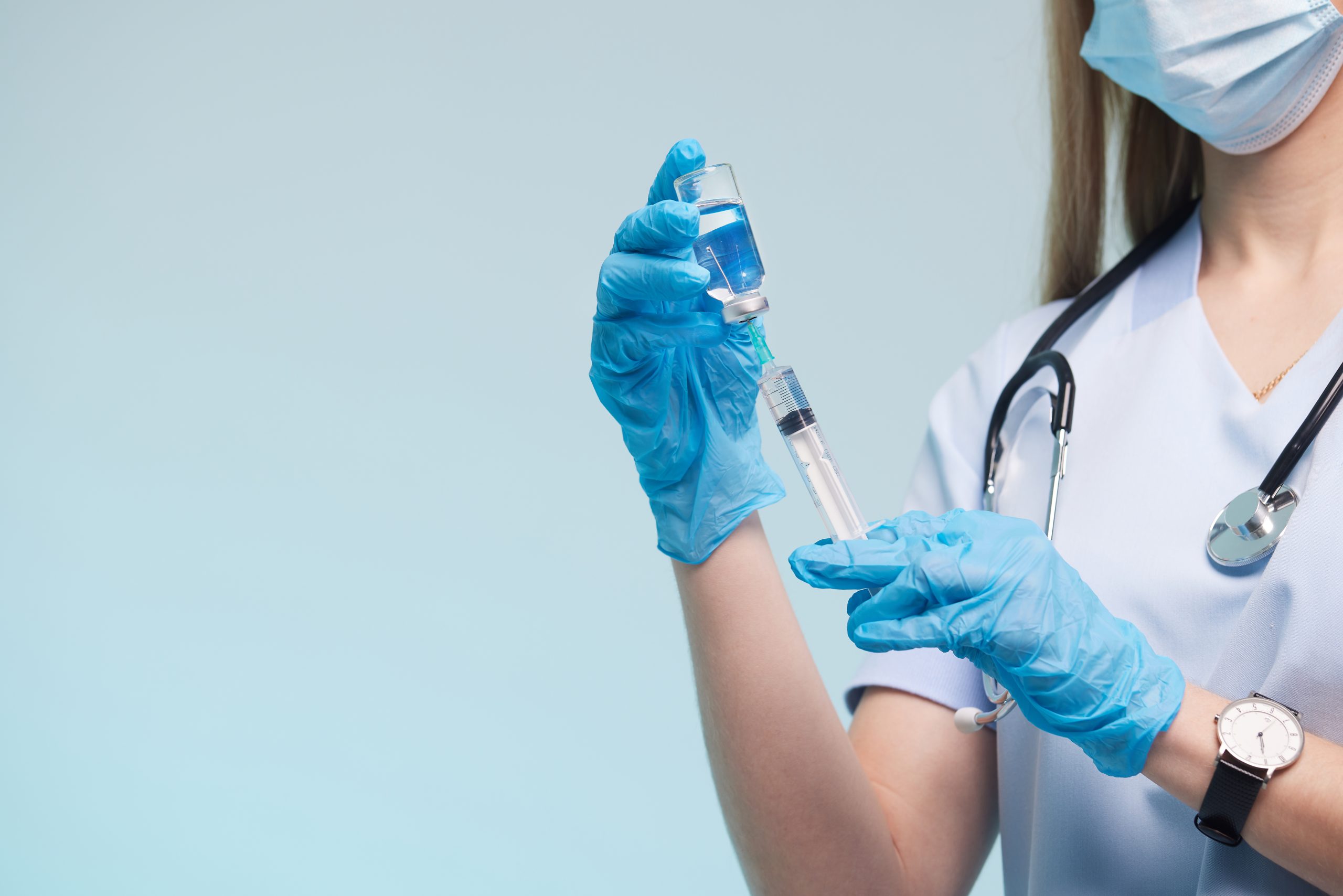 The doctor's hand wears a medical glove holding a syringe while taking a liquid vaccine from a vial about to be injected. Injection vaccination concept
