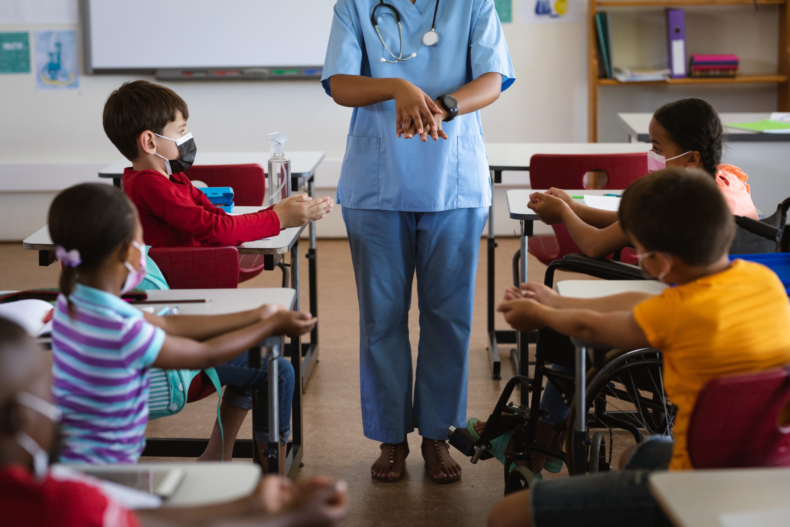 Mid section of female health worker showing students to use hands sanitizer at elementary school. education back to school health safety during covid19 coronavirus pandemic.